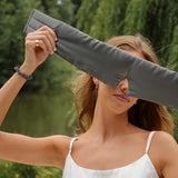 Model wearing the Silk Works Cloud Eye Mask in grey, styled with a white silk camisole and matching grey silk scrunchie. Photographed in a serene natural setting.