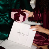 Person in green silk pyjamas outfit receiving a pink gift box with a bow from another person, with Silk Works London packaging.