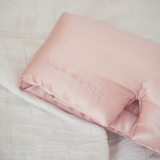 Pink pillow eye mask with 'SILK WORKS' branding on a soft surface