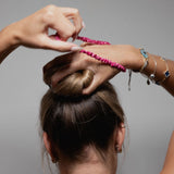Woman styling her hair into a bun using a hot pink Silk Works mulberry silk scrunchie, showcasing gentle hold and frizz-free styling.