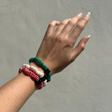 Hand wearing ivory, jade and watermelon pink silk skinny scrunchies on a plain background