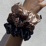 Set of three silk scrunchies on wrist in leopard print, caramel, and black – soft, elegant, and perfect for a gentle, crease-free hold.
