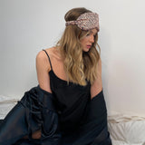 Model wearing a Silk Works leopard print mulberry silk eye mask with ruched strap, styled in loose waves and a black silk cami set and robe.