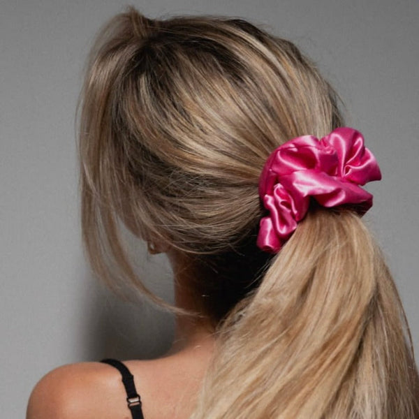 Model with long blonde hair tied in a ponytail using a hot pink mulberry silk scrunchie by Silk Works London; gentle, luxury hair accessory designed to prevent breakage and reduce frizz.