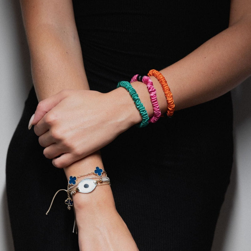 Image of a model wearing a set of three luxury silk hair ties in green, pink, and orange, by Silk Works London. Soft mulberry silk small scrunchies designed to prevent hair damage and reduce frizz.