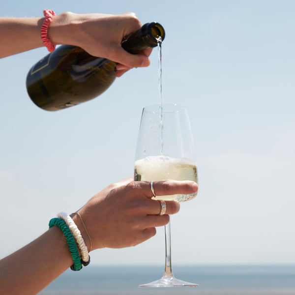 Someone pouring a glass of wine with three silk scrunchies on their wrist.