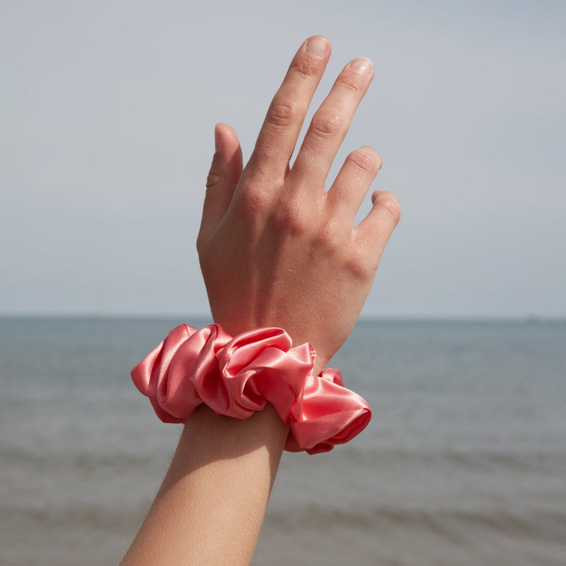 Hand wearing a large watermelon pink silk scrunchie on the wrist – showcasing its soft texture and elegant, oversized design