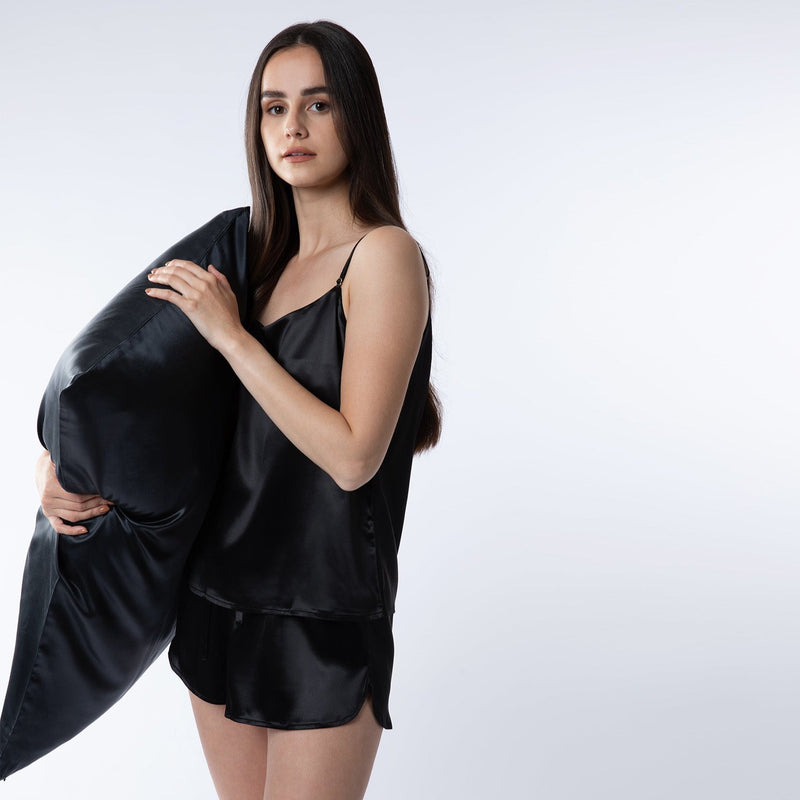 Lady wearing black silk shorts and cami top holding a black silk pillowcase