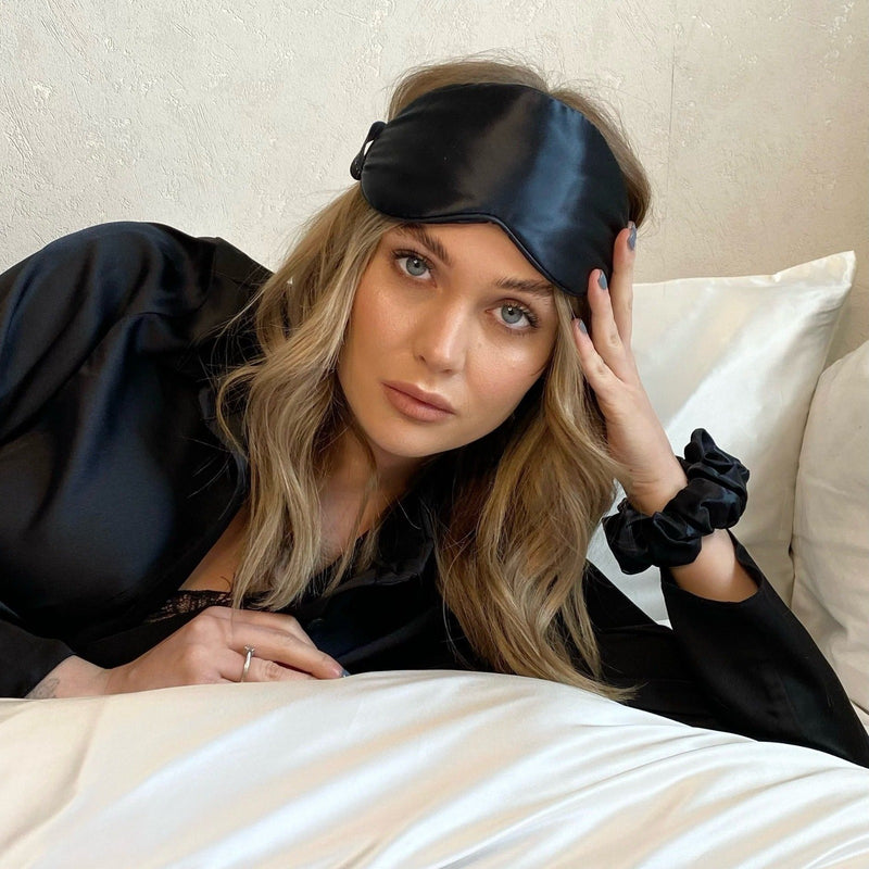 Lady lying on bed wearing a black silk eye mask, scrunchie and robe