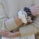 Large silk scrunchies in neutral tones—caramel, grey, and ivory—styled on a model’s wrist, highlighting their soft texture and elegant volume