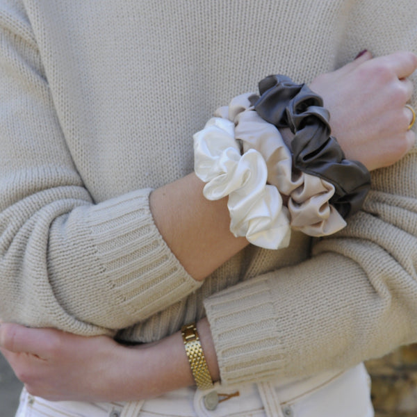 Large silk scrunchies in neutral tones—caramel, grey, and ivory—styled on a model’s wrist, highlighting their soft texture and elegant volume